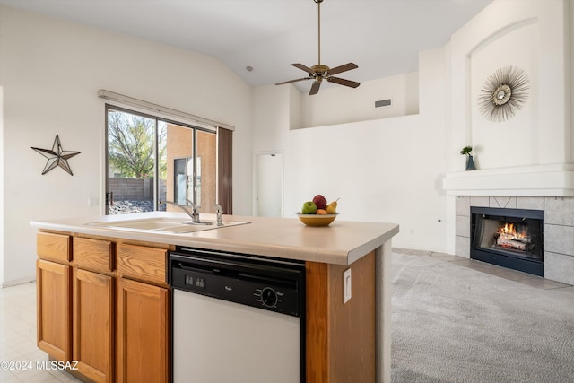 kitchen featuring a tile fireplace, dishwasher, sink, an island with sink, and vaulted ceiling