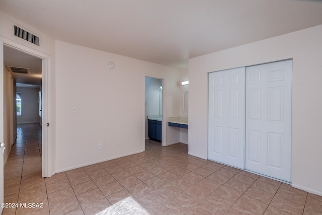 unfurnished bedroom featuring a closet, ensuite bathroom, and light tile patterned floors