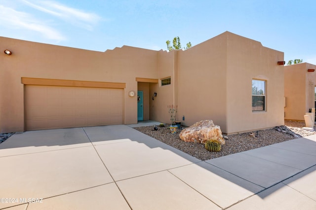 pueblo-style house with stucco siding, an attached garage, and driveway