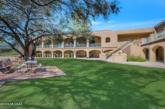 rear view of house featuring a yard, a patio area, a balcony, and stucco siding