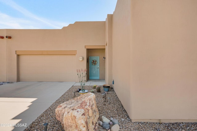 property entrance with stucco siding, an attached garage, and driveway