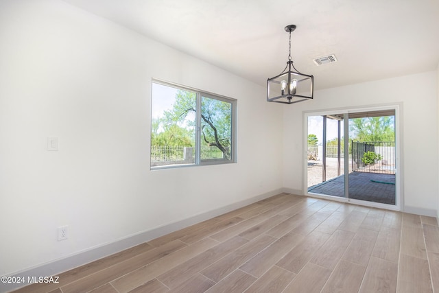 empty room with a notable chandelier and light hardwood / wood-style floors