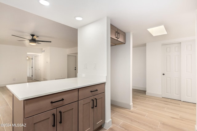 kitchen featuring ceiling fan, a skylight, light hardwood / wood-style floors, and kitchen peninsula