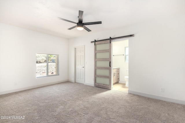 unfurnished bedroom with a barn door, ceiling fan, light colored carpet, and ensuite bath