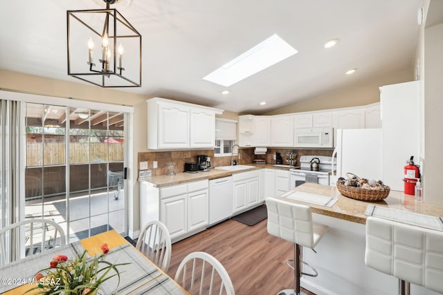 kitchen with decorative backsplash, sink, lofted ceiling with skylight, white cabinetry, and white appliances