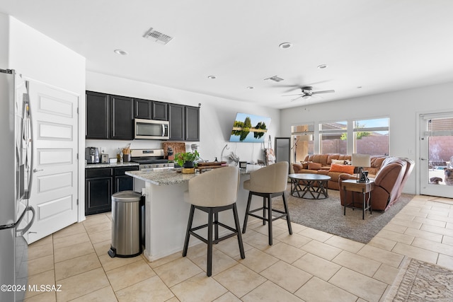 kitchen with light stone countertops, ceiling fan, a breakfast bar, appliances with stainless steel finishes, and a center island with sink