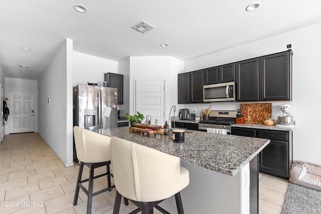 kitchen with appliances with stainless steel finishes, dark stone countertops, a kitchen island with sink, and a kitchen bar