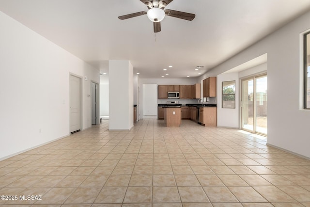 kitchen with dark countertops, stainless steel microwave, open floor plan, a center island, and a sink