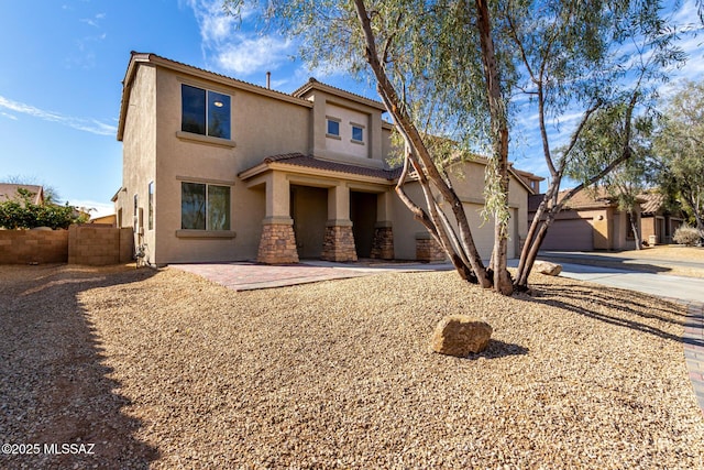 view of front of home with driveway, stone siding, an attached garage, fence, and stucco siding