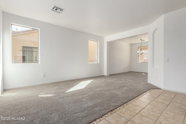 spare room with light carpet, a notable chandelier, and visible vents