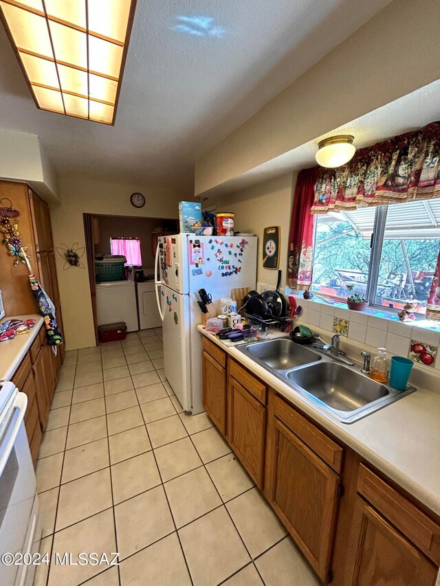 kitchen featuring washer and dryer, sink, light tile patterned floors, and white appliances