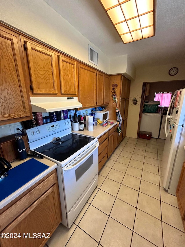 kitchen featuring washer / dryer, light tile patterned flooring, and white appliances