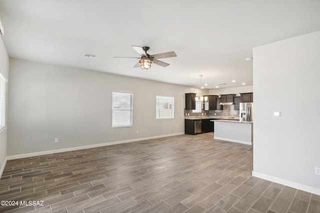 unfurnished living room with ceiling fan with notable chandelier and dark hardwood / wood-style floors