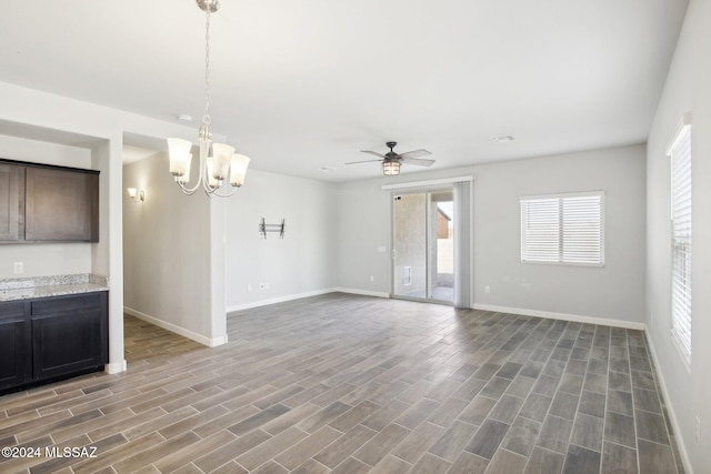 unfurnished living room with ceiling fan with notable chandelier and dark hardwood / wood-style flooring