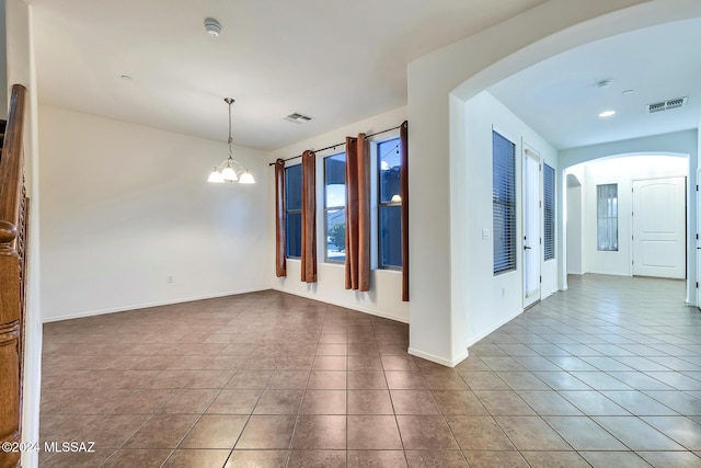 tiled spare room with a chandelier