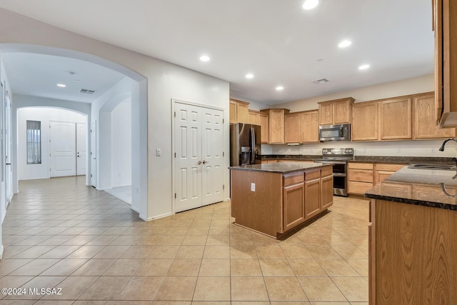 kitchen featuring appliances with stainless steel finishes, a center island, dark stone countertops, and sink