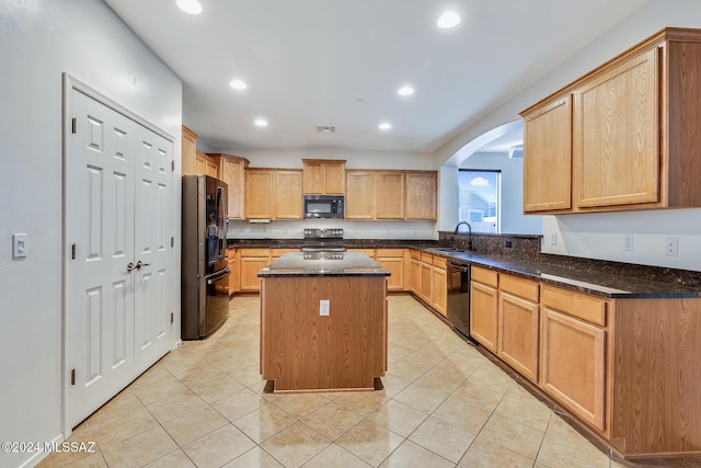 kitchen with a center island, sink, dark stone countertops, light tile patterned floors, and black appliances