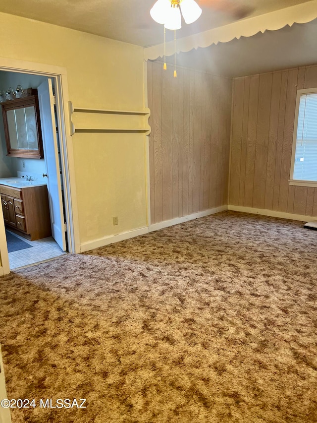 carpeted spare room featuring wooden walls, sink, and ceiling fan