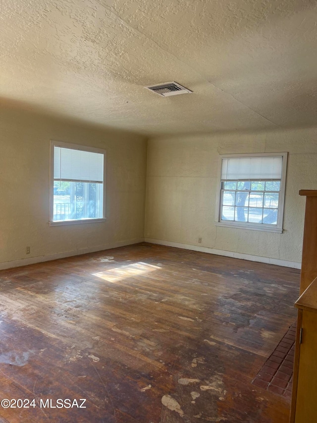 unfurnished room featuring a wealth of natural light, a textured ceiling, and dark hardwood / wood-style flooring