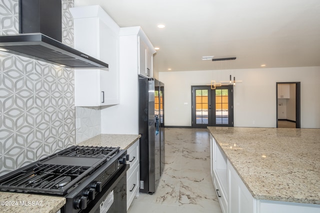 kitchen featuring french doors, wall chimney exhaust hood, hanging light fixtures, and white cabinetry