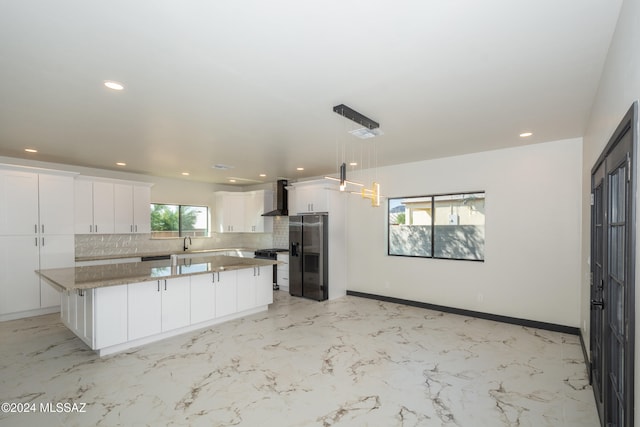 kitchen with a kitchen island, tasteful backsplash, wall chimney exhaust hood, white cabinetry, and decorative light fixtures