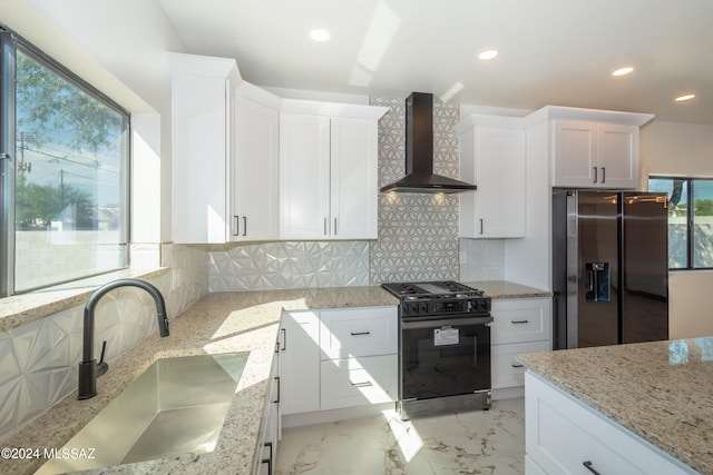 kitchen featuring stainless steel fridge, black range with gas stovetop, wall chimney range hood, white cabinetry, and backsplash