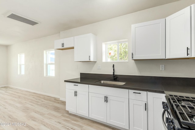 kitchen with white cabinets, light hardwood / wood-style flooring, stainless steel gas range, and sink