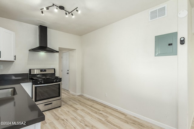 kitchen featuring wall chimney exhaust hood, electric panel, light hardwood / wood-style floors, stainless steel gas range, and white cabinetry