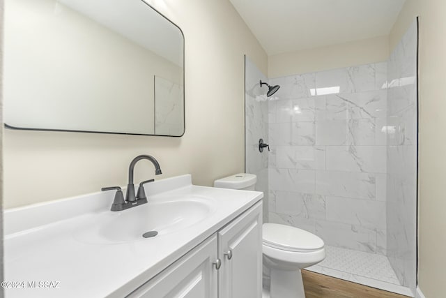 bathroom featuring wood-type flooring, a tile shower, vanity, and toilet