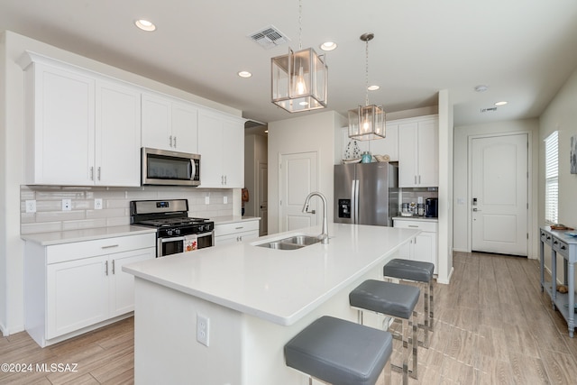 kitchen with a kitchen island with sink, stainless steel appliances, sink, pendant lighting, and white cabinets