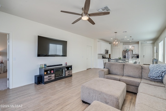 living room with ceiling fan with notable chandelier and light hardwood / wood-style floors