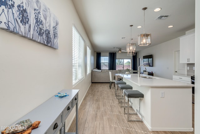 kitchen featuring an island with sink, a kitchen breakfast bar, an inviting chandelier, white cabinetry, and decorative light fixtures