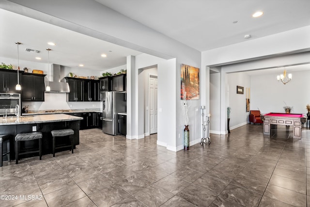 kitchen with wall chimney exhaust hood, light stone countertops, stainless steel appliances, and pendant lighting