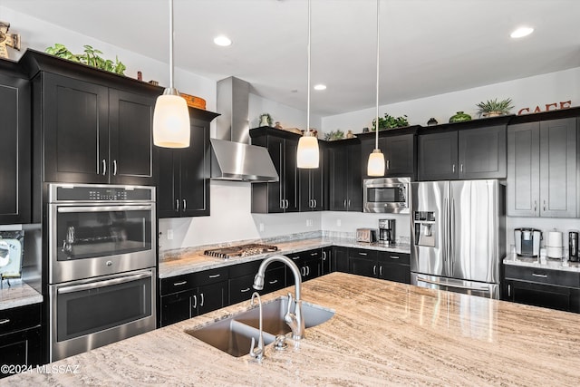 kitchen featuring wall chimney exhaust hood, hanging light fixtures, sink, light stone countertops, and appliances with stainless steel finishes