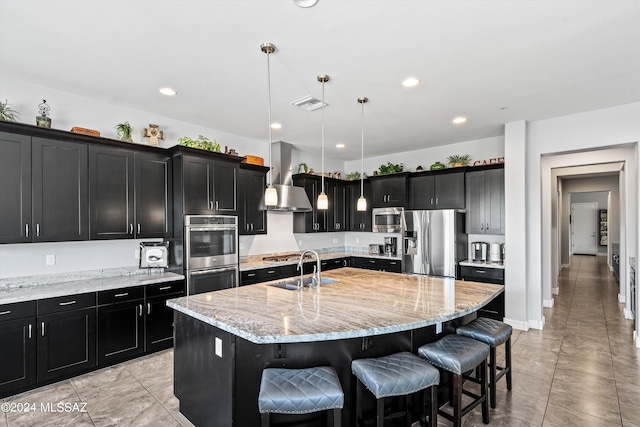 kitchen with a breakfast bar area, a center island with sink, decorative light fixtures, appliances with stainless steel finishes, and light stone counters