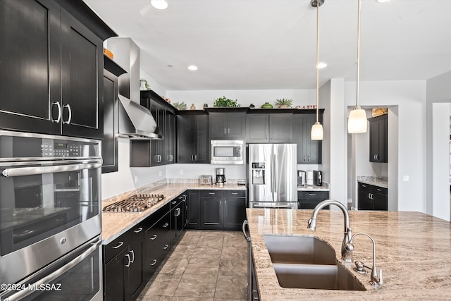 kitchen with wall chimney range hood, stainless steel appliances, sink, pendant lighting, and light stone counters