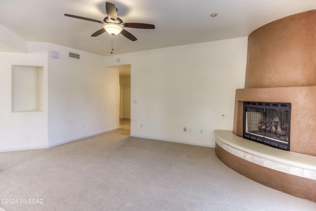 unfurnished living room with a large fireplace, carpet flooring, and ceiling fan