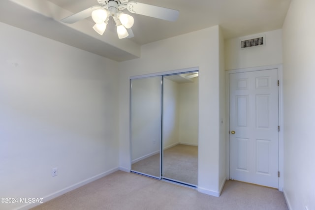 unfurnished bedroom with a closet, light colored carpet, and ceiling fan