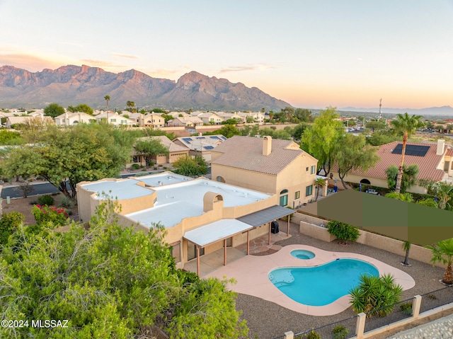 pool at dusk featuring a patio, a mountain view, and an in ground hot tub