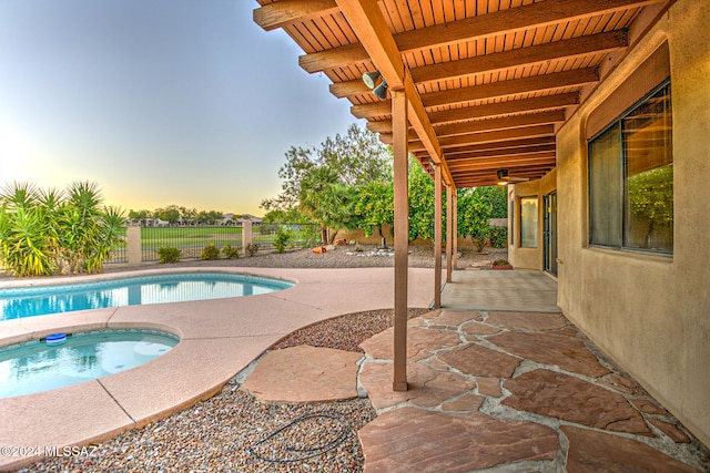 pool at dusk featuring a patio area and an in ground hot tub