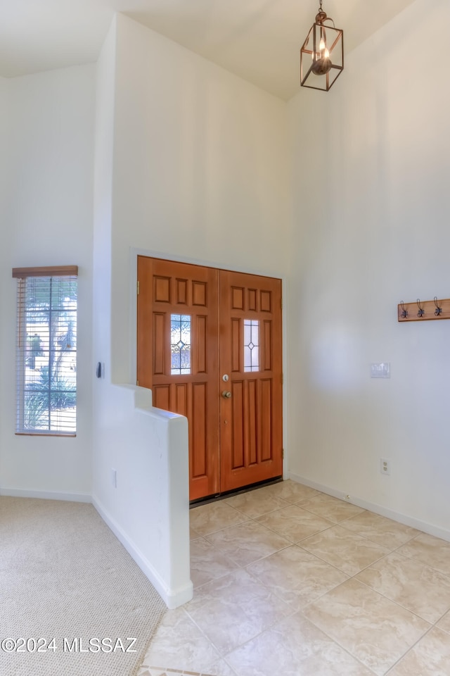 foyer entrance with light carpet, a chandelier, and a high ceiling