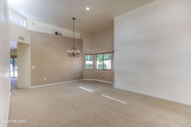 empty room featuring light carpet, a towering ceiling, and an inviting chandelier