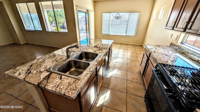 kitchen featuring a healthy amount of sunlight, sink, black gas range, and an island with sink