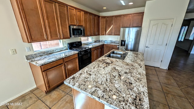 kitchen with light stone countertops, appliances with stainless steel finishes, sink, and a center island with sink