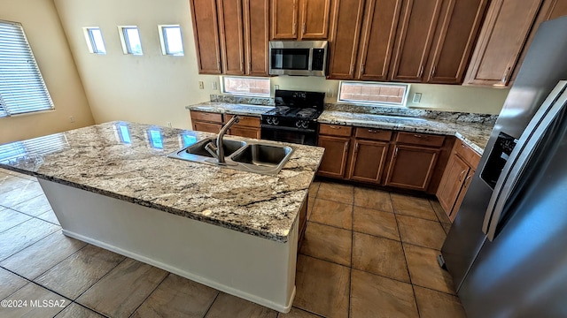 kitchen with appliances with stainless steel finishes, a kitchen island with sink, sink, and light stone counters