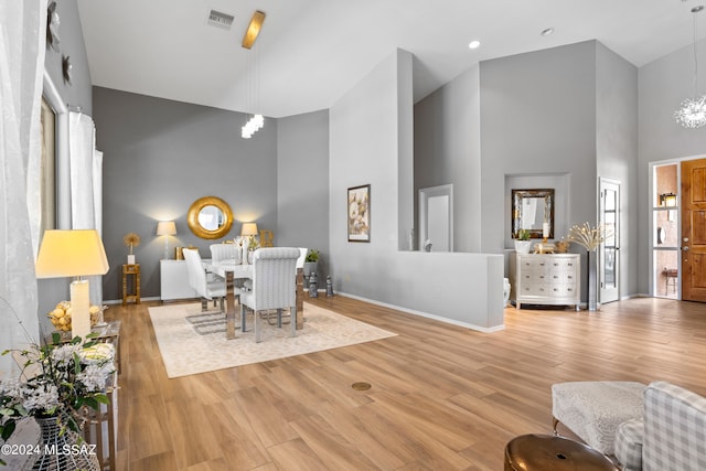 dining area with an inviting chandelier, high vaulted ceiling, and light hardwood / wood-style flooring