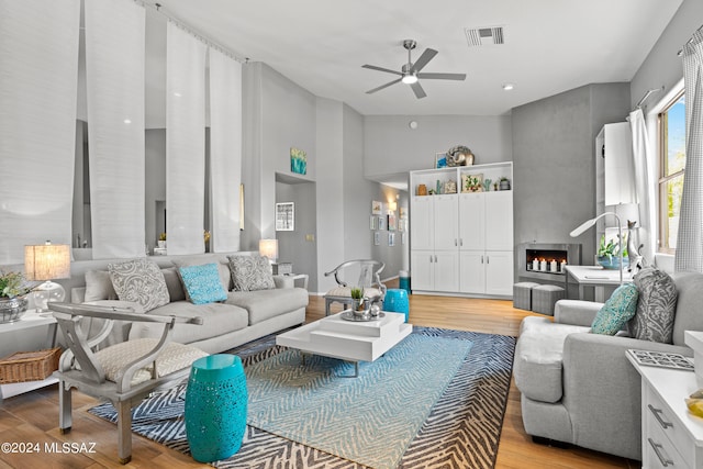 living room with a fireplace, high vaulted ceiling, light wood-type flooring, and ceiling fan