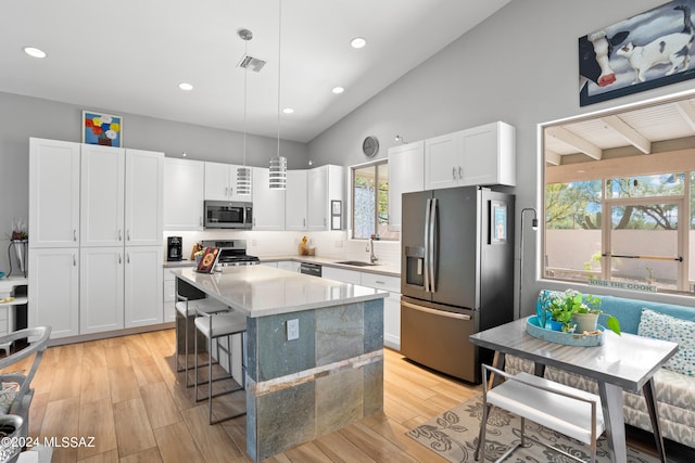 kitchen featuring hanging light fixtures, sink, a kitchen island, appliances with stainless steel finishes, and light hardwood / wood-style floors