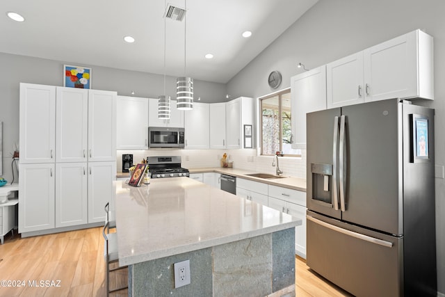 kitchen featuring stainless steel appliances, sink, light hardwood / wood-style floors, pendant lighting, and white cabinetry