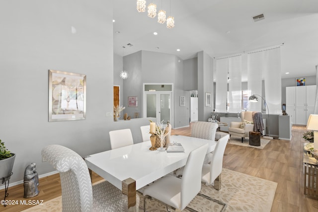 dining space with light wood-type flooring and a towering ceiling